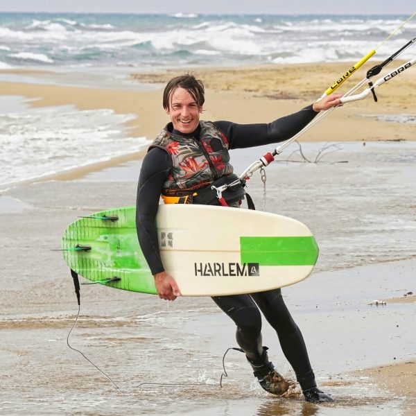 Joel mit einem Kitesurfboard unter dem Arm läuft am Strand