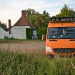 orangener Sprintercampervan parkt vor englischem Pub